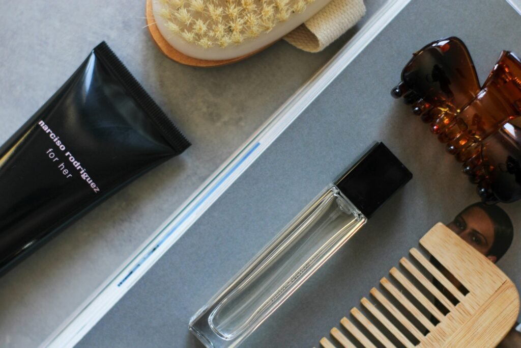 Stylish flat lay of beauty essentials including comb, brush, hair clip, perfume, and body lotion.